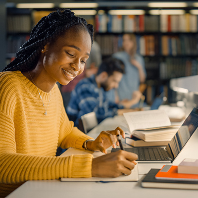 University Library: Gifted Black Girl uses Laptop, Writes Notes for the Paper, Essay, Study for Class Assignment. Diverse Multi-Ethnic Group of Students Learning, Studying for Exams, Talk in College